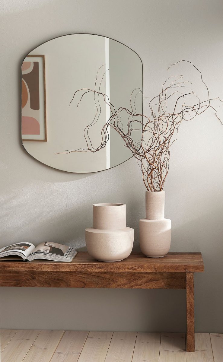 Sittbänk i trendigt trä med spegel ovanför och vaser.